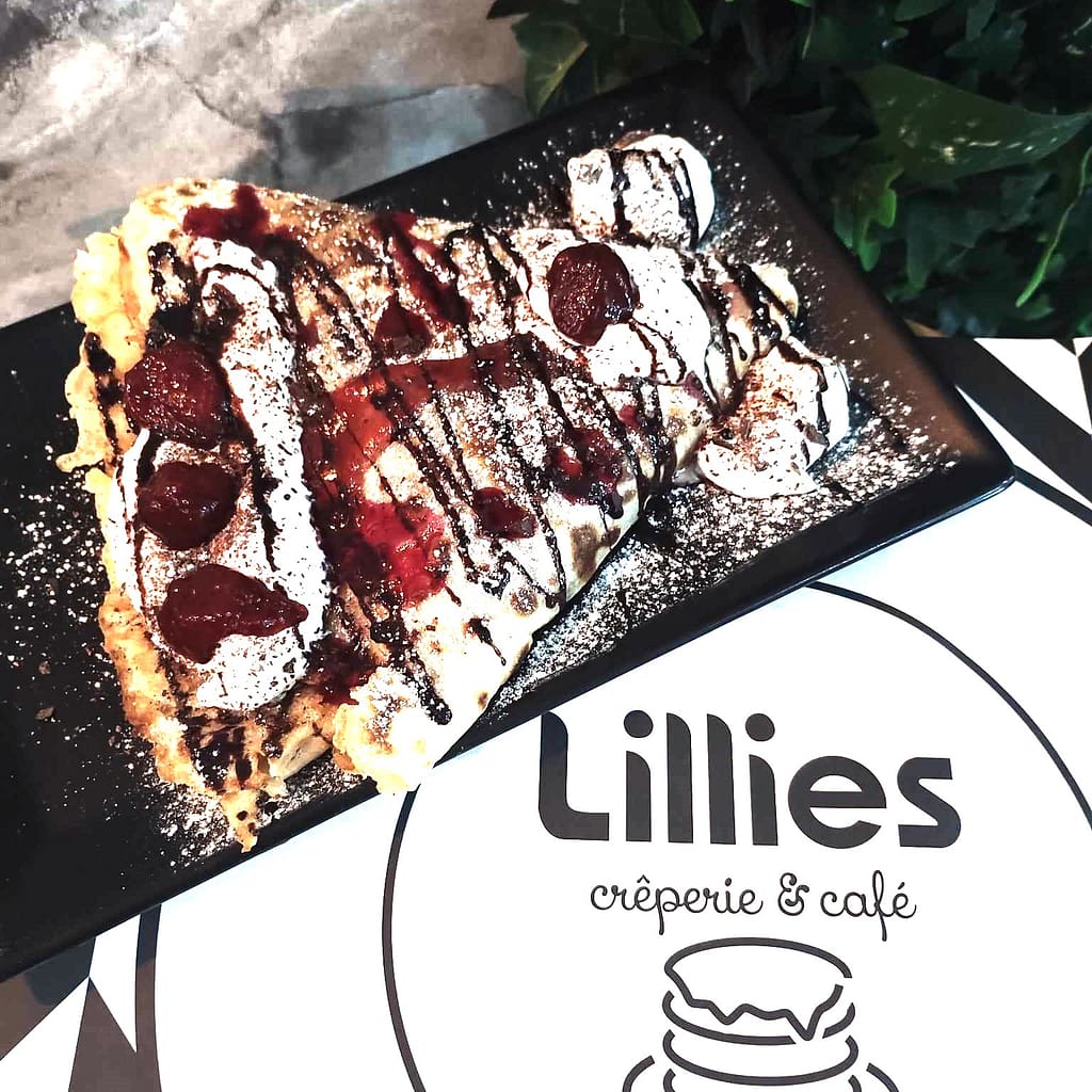 Delicious crepe with cherry compote, chocolate drizzle, and powdered sugar at Lillies Creperie & Café in Belgrade. Perfect dessert treat in a cozy café setting.